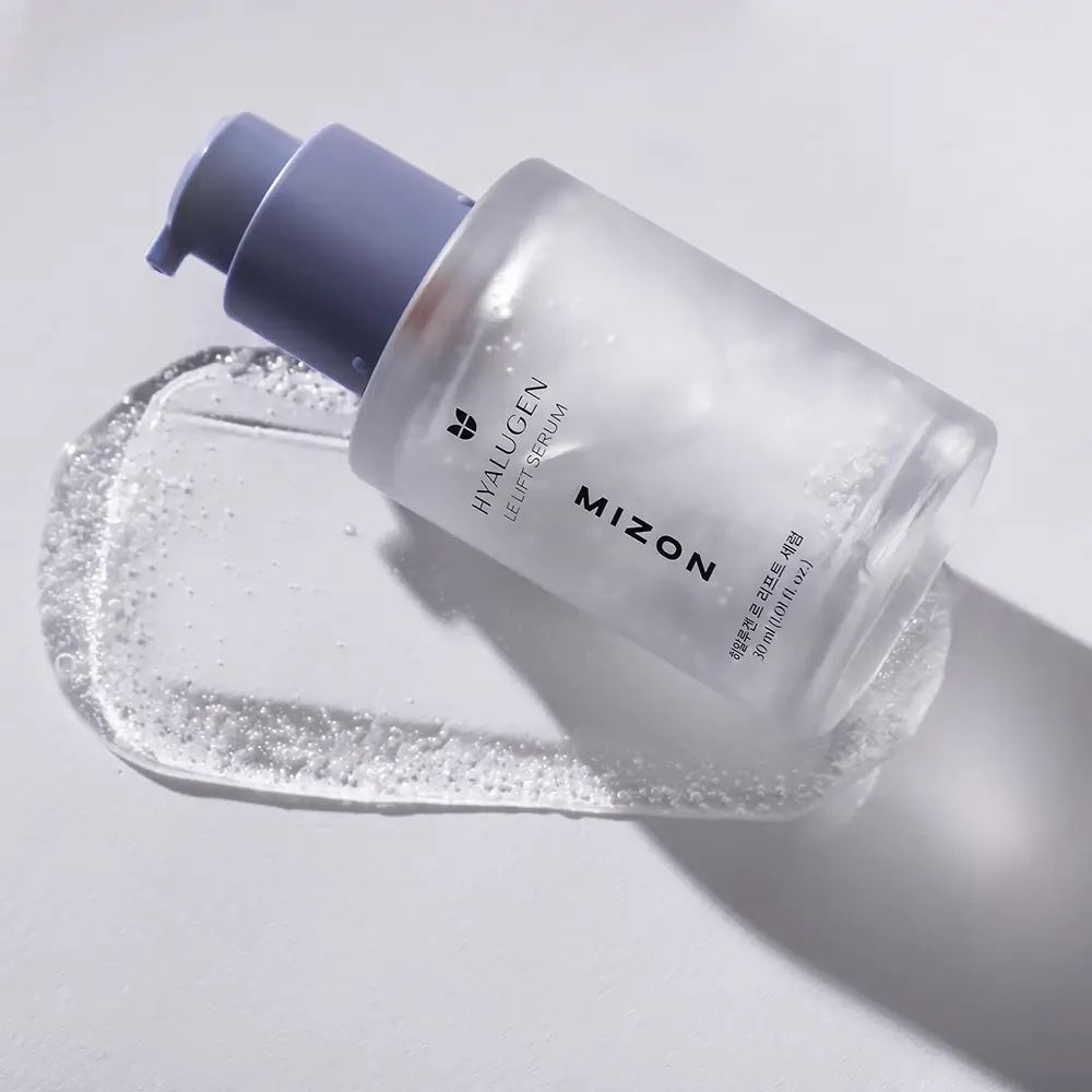 Serumflakon liegt auf einer Serumspur. Aufschrift: Hyalugen Le Lift Serum, Mizon. Transparentes Serum.