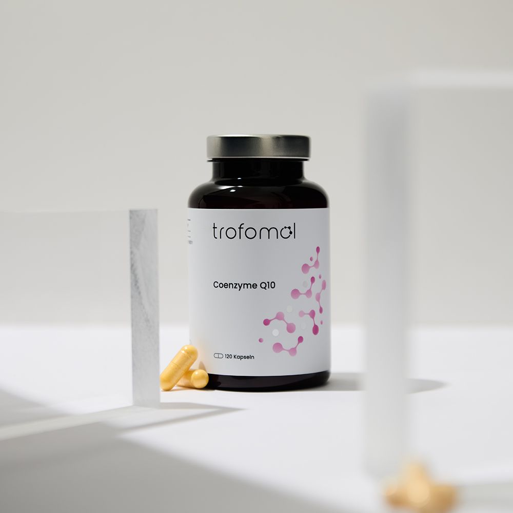 Braune Glasflasche mit weißem Etikett. Aufschrift: trofomol, Coenzyme Q10. Daneben Kapseln und ein Stück Papier.