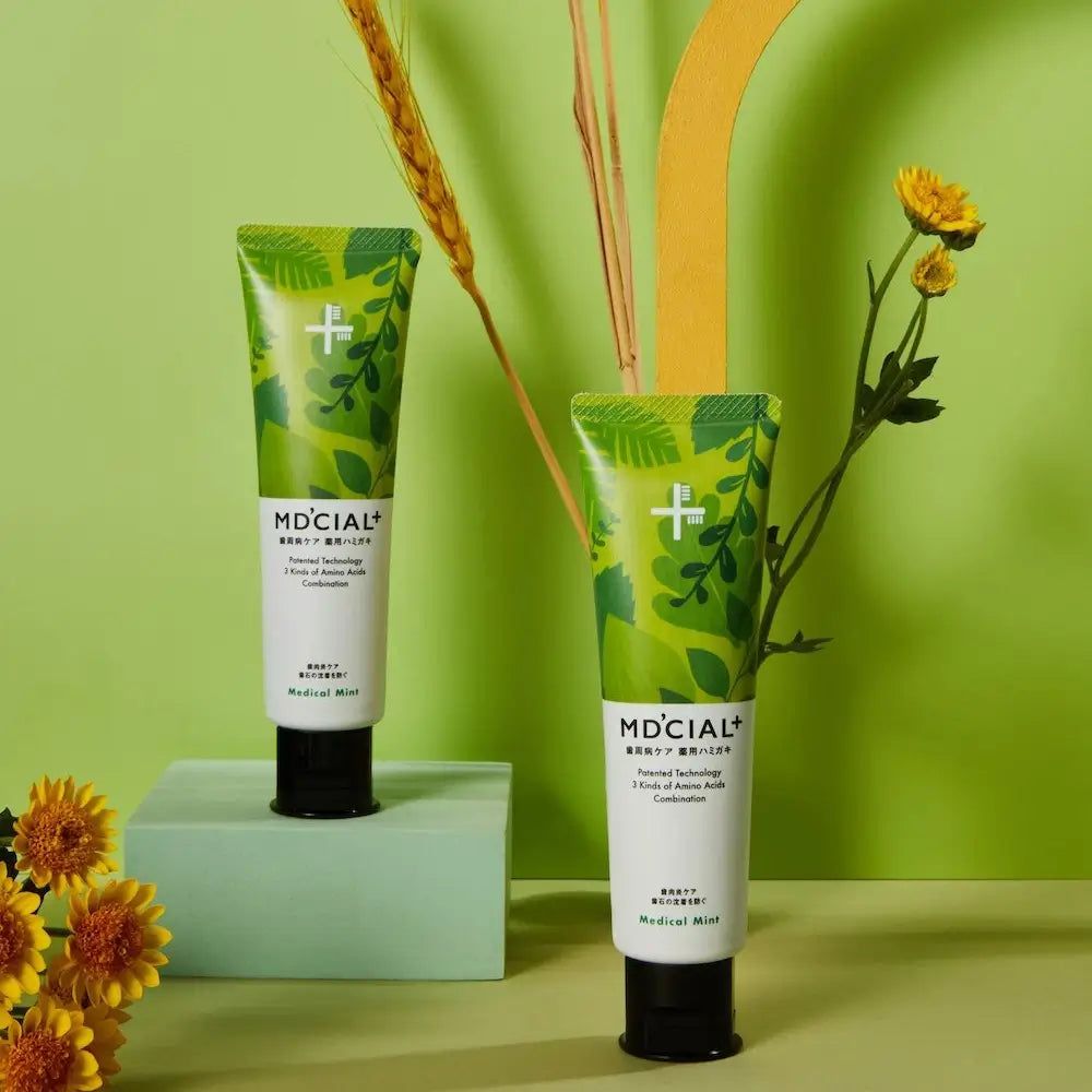 Zwei MD'CIAL+ Zahncreme-Tuben. Grünes Design, Schriftzug Medical Mint. Schwarzer Verschluss. Dekoration mit Blumen.