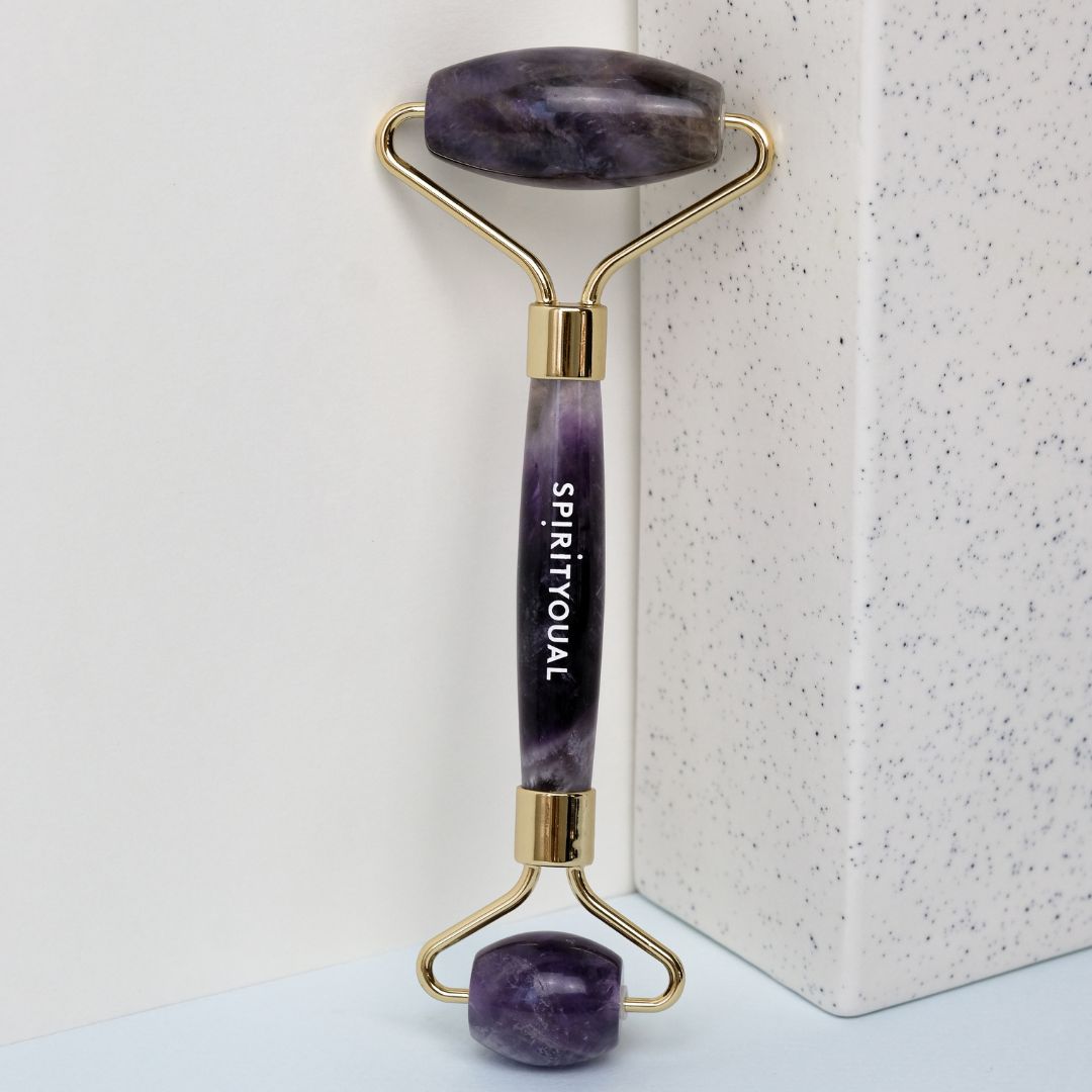 Amethyst-Gesichtsroller mit goldenem Rahmen. Der Griff trägt den Schriftzug SPIRITYOUAL. Auf hellem Hintergrund.