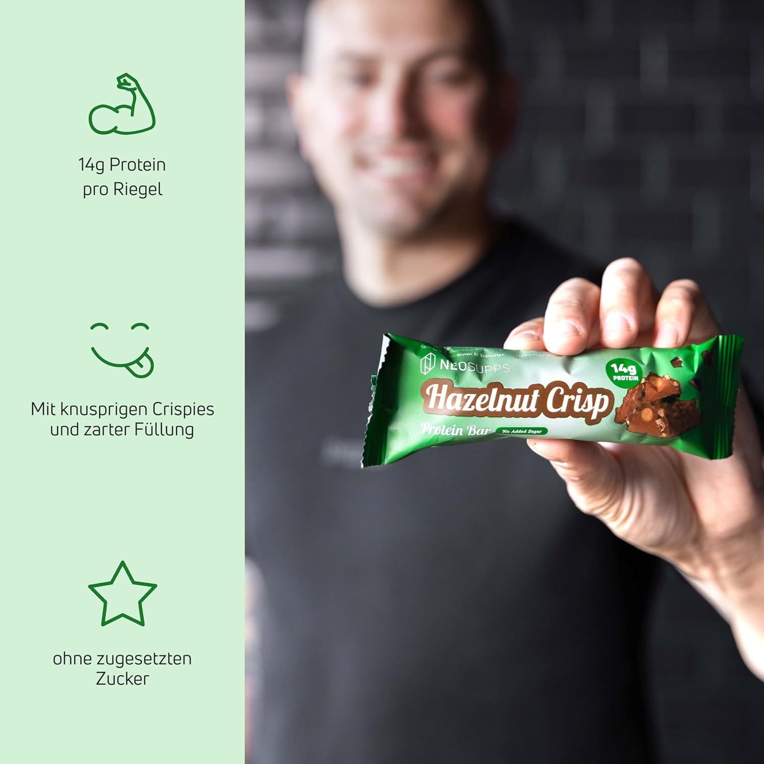 Eine Person hält eine grüne Proteinriegel-Verpackung mit der Aufschrift "Hazelnut Crisp". Auf der Verpackung steht "14g Protein".
