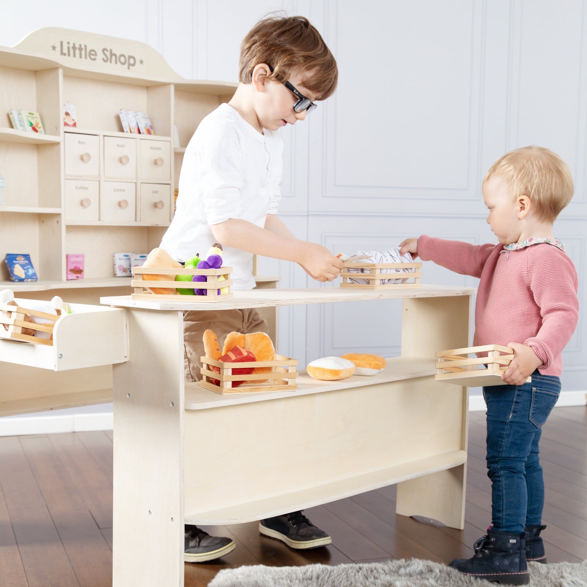 Holz-Verkaufsstand mit Regalen, Theke und Schubladen. Kinder spielen mit Spielzeug-Lebensmitteln in Körben.