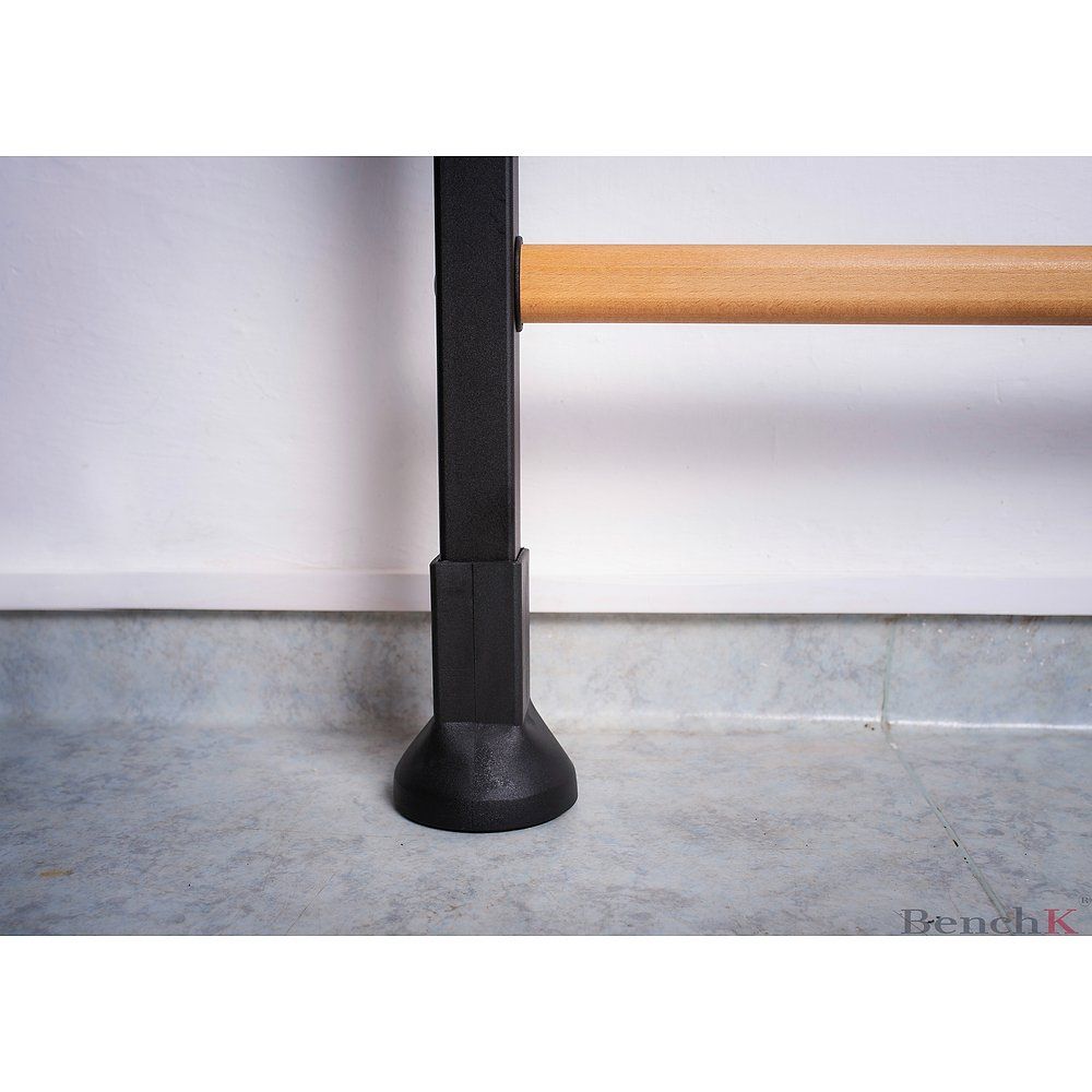 Schwarzer Metallrahmen mit Holzstange. BenchK-Logo unten rechts. Bodenkontakt durch schwarzen Fuß.