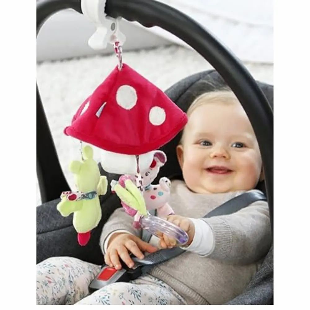 Baby im Autositz mit Mobile. Mobile mit Pilz, Reh und Frosch. Baby lächelt im Autositz.
