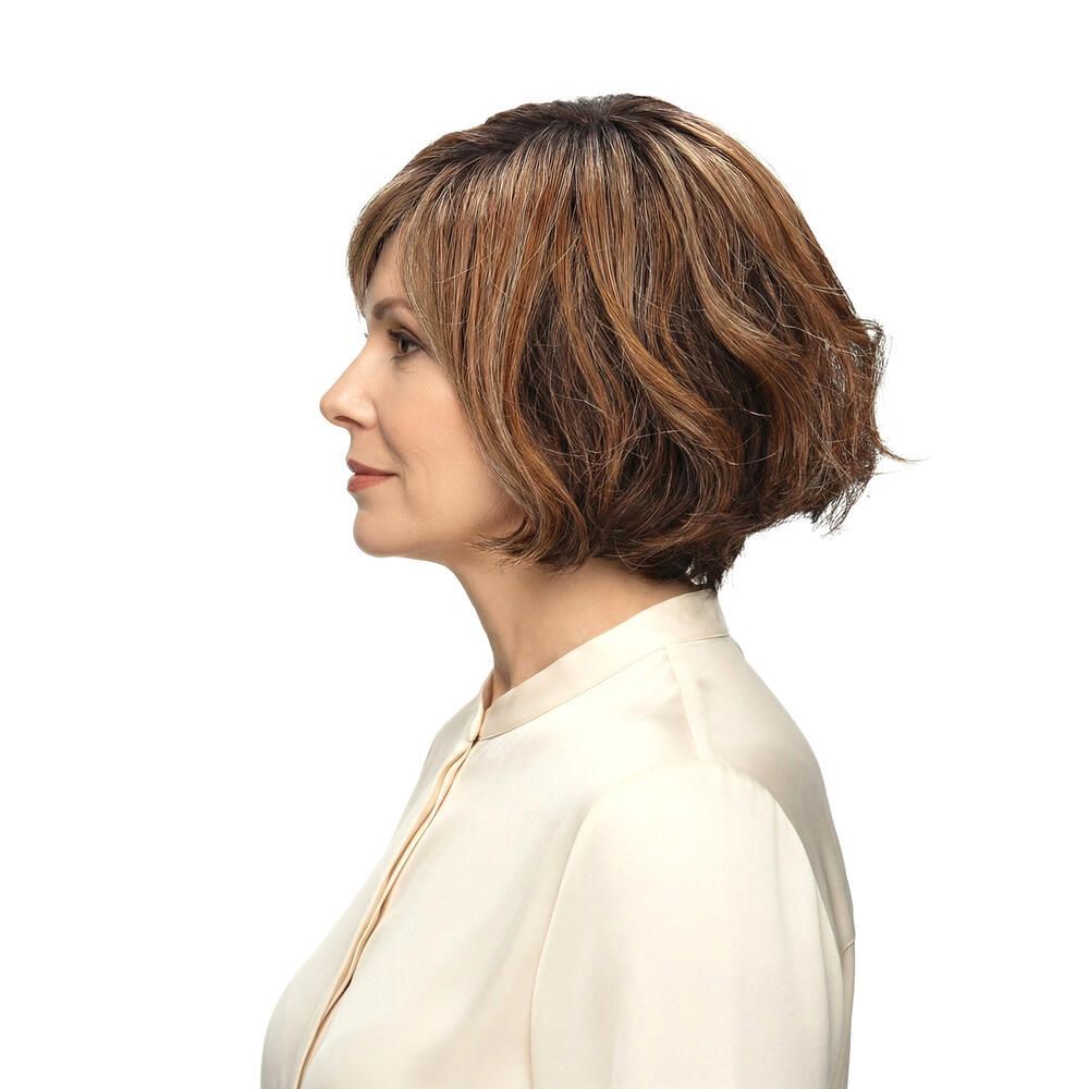 Frau mit brauner Perücke mit Pony. Die Perücke hat blonde Strähnen und welliges Haar. Sie trägt ein weißes Hemd.