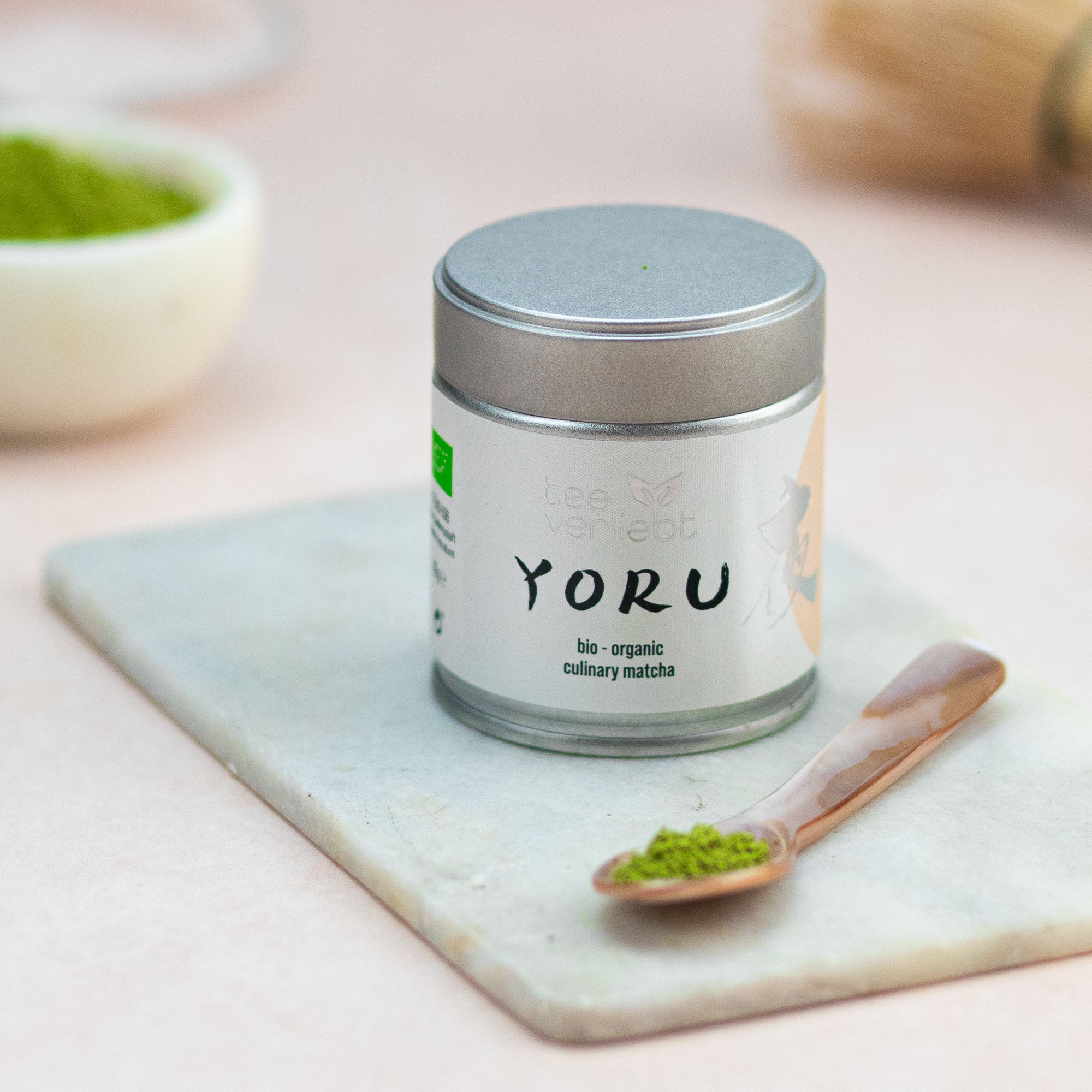 Dose Yoru Culinary Matcha auf Marmorplatte. Löffel mit Matcha. Schale mit Matcha-Pulver. Hintergrund unscharf.