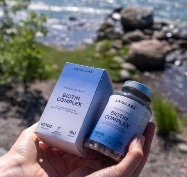 Hände halten Flasche und Karton des Biotin Komplex Nahrungsergänzungsmittels am Wasser.