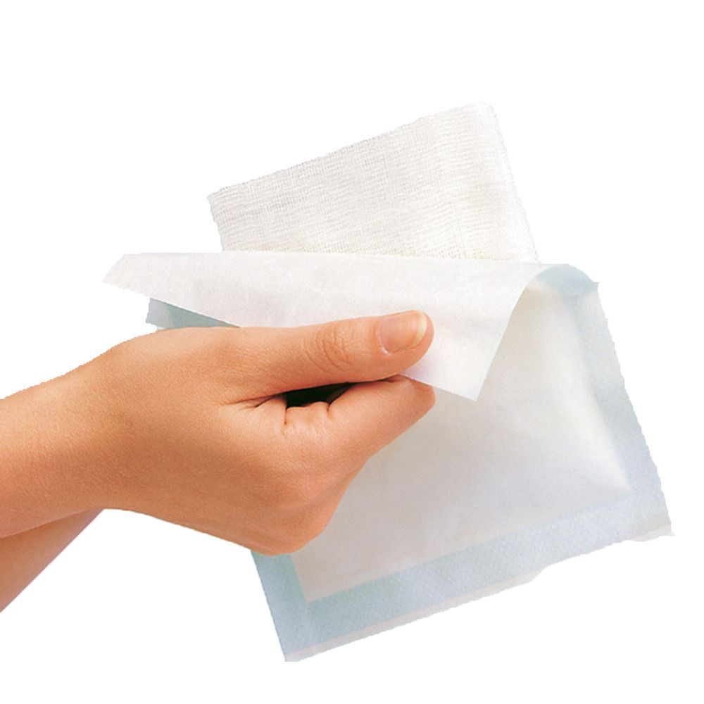 Hand hält sterile Kompressen. Mehrere weiße, rechteckige Kompressen, teilweise entfaltet, liegen auf einer blauen Verpackung.