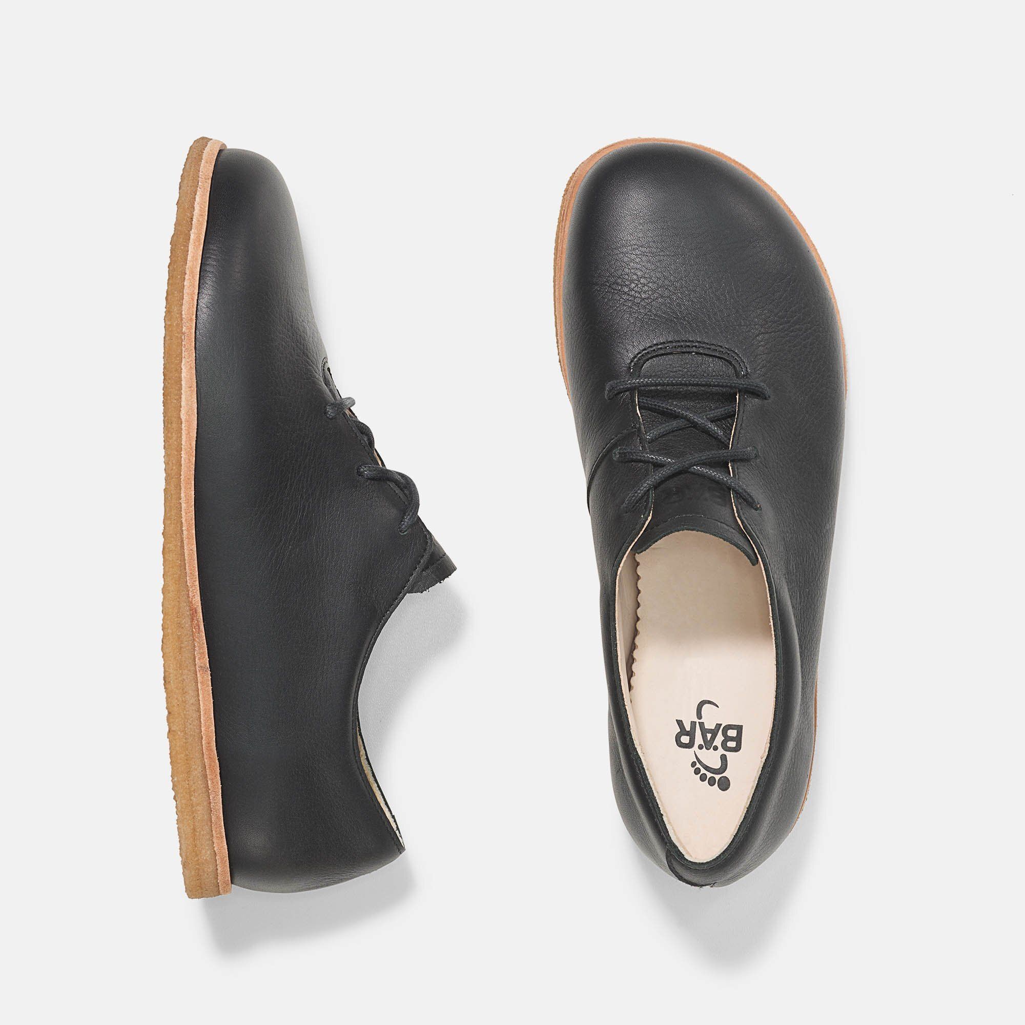 Zwei Schuhe: einer von oben, einer von der Seite. Schwarzes Leder, helle Sohle. Innensohle mit Logo.