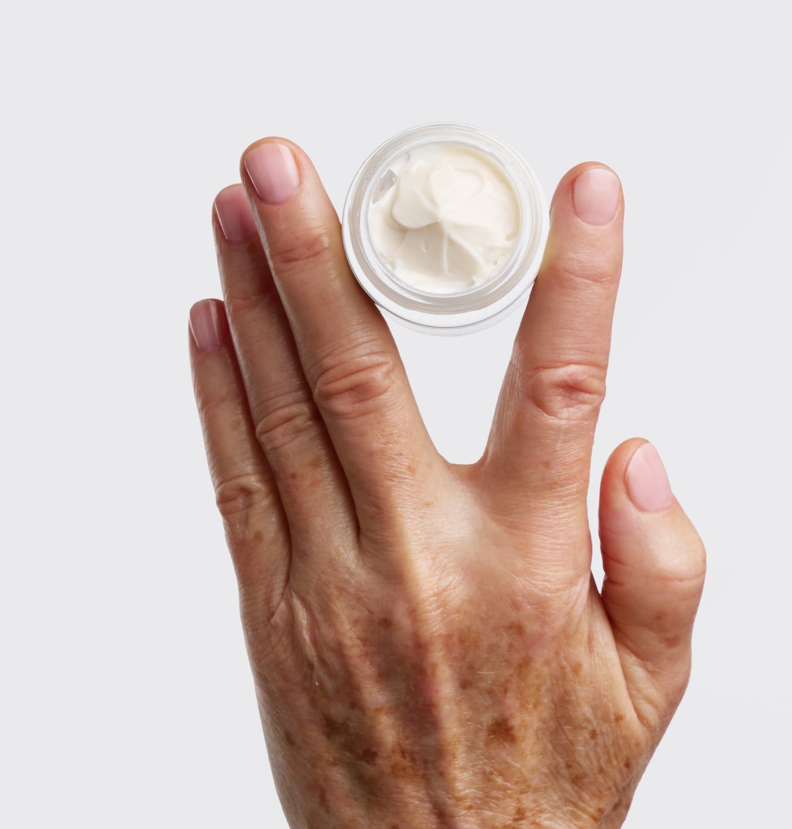 Hand hält einen offenen Tiegel mit cremiger Substanz. Der Tiegel ist transparent.