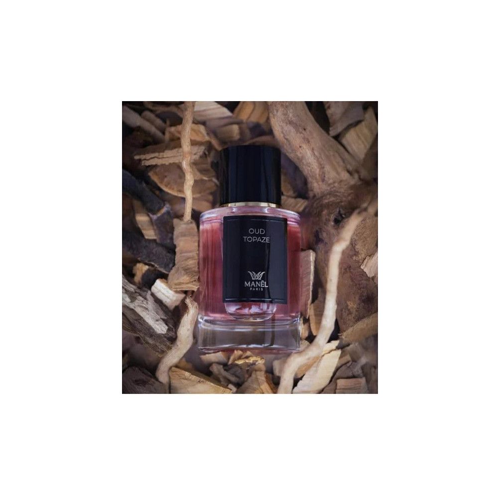 Parfumflakon mit schwarzem Deckel und Etikett. Aufschrift Oud Topaze und Manel Paris. Auf Holzstücken platziert.