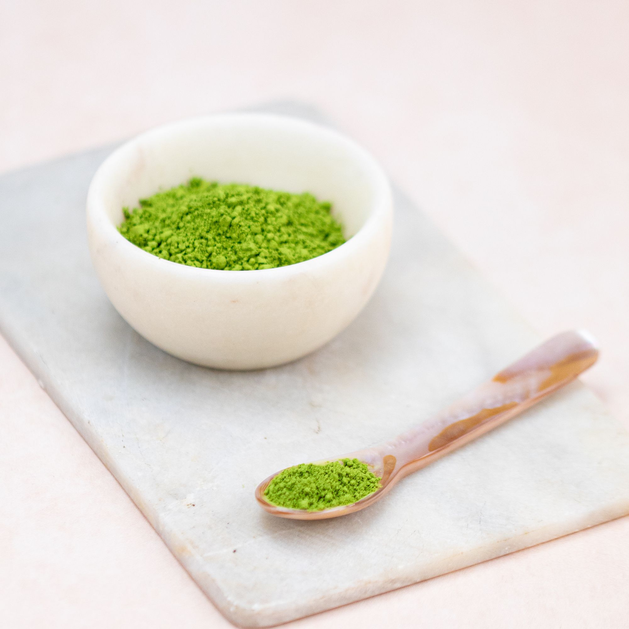 Kleine Schale mit Matcha-Pulver. Löffel mit Matcha-Pulver. Auf Steinplatte. Hintergrund rosa.