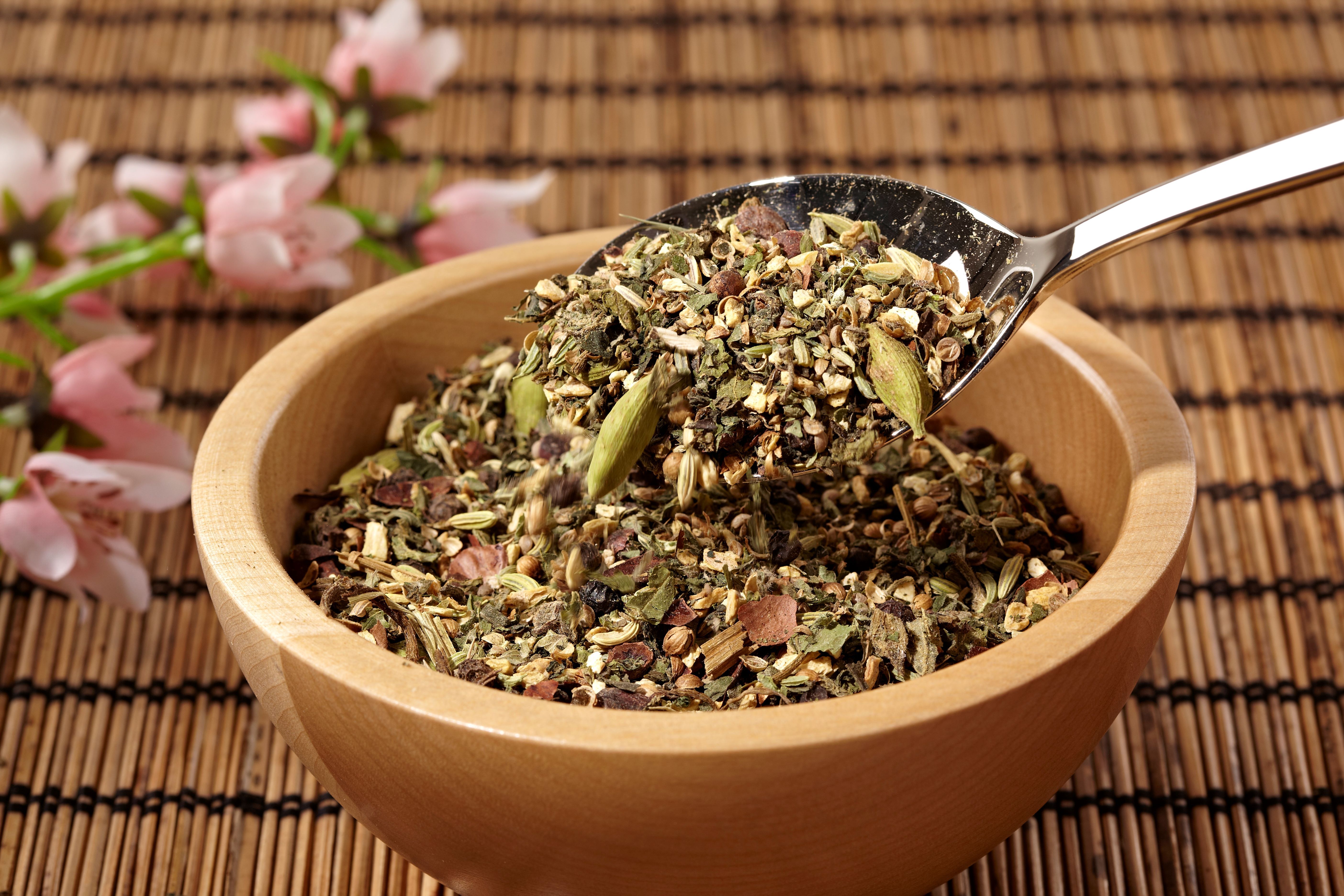 Holzschale mit Kräutermischung. Ein Löffel hebt die Mischung an. Auf Bambusmatte.