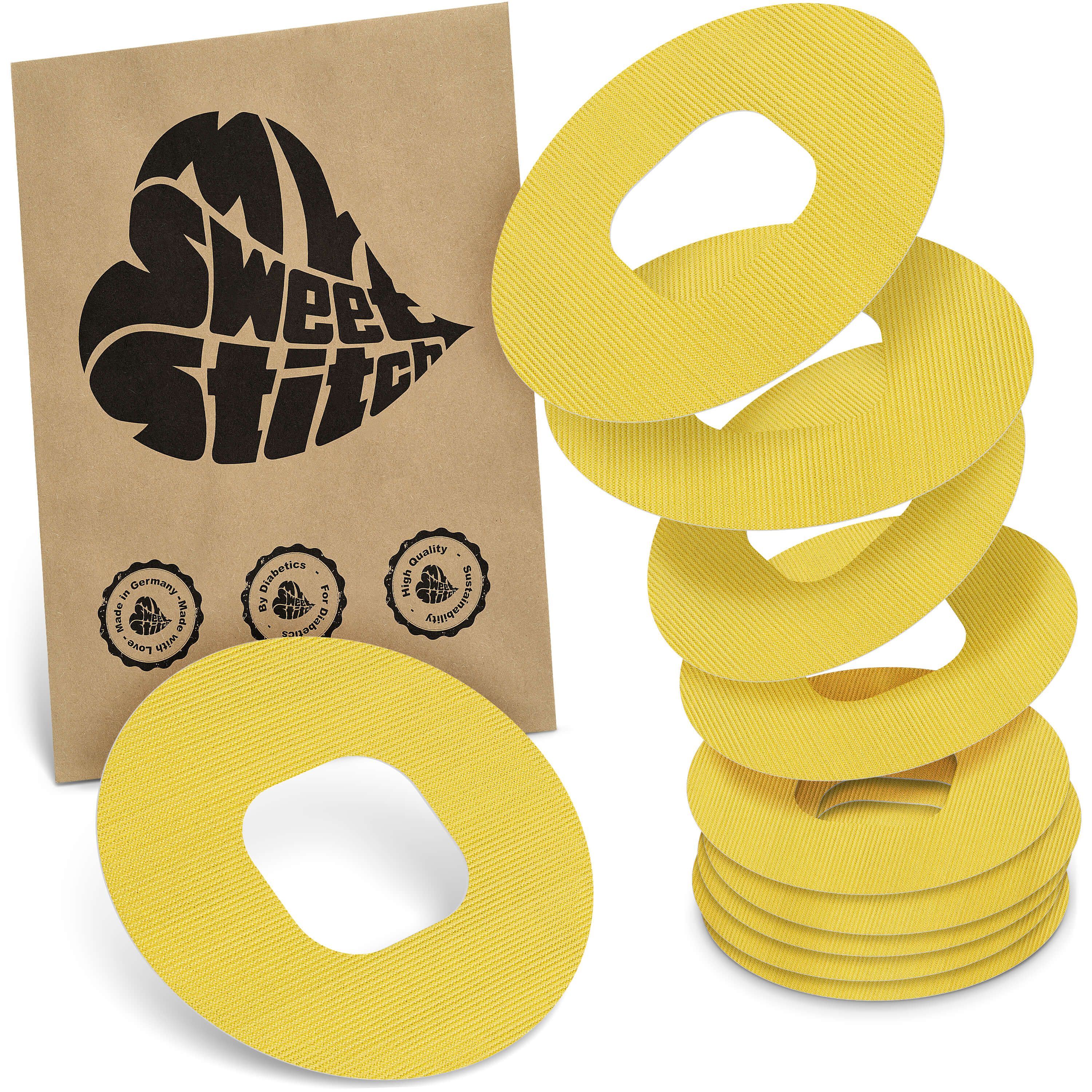 Gelbe, ringförmige Pflaster mit Loch in der Mitte. Auf brauner Verpackung steht "My Sweet Stitch". Mehrere Pflaster sind gestapelt.