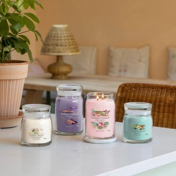 Vier Kerzen in Gläsern auf einem Tisch. Verschiedene Farben und Aufschriften. Umgebung: Topf, Tisch, Stuhl, Lampe.