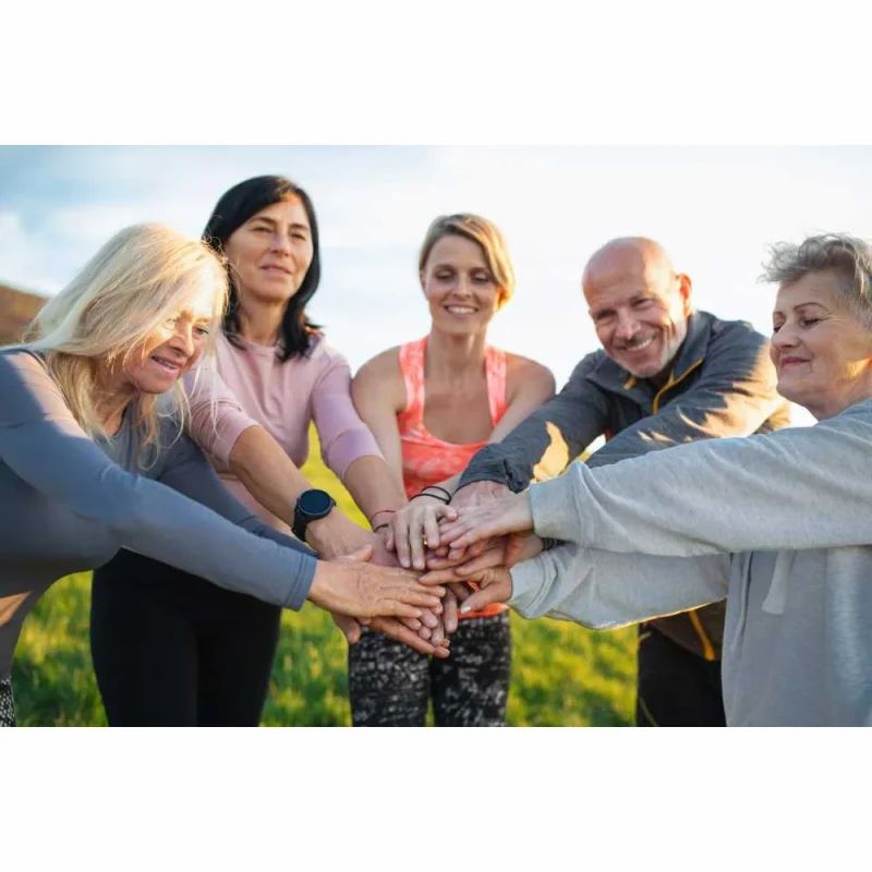 Gruppe von Menschen legt Hände zusammen. Helle Kleidung, im Freien, sonniges Wetter.