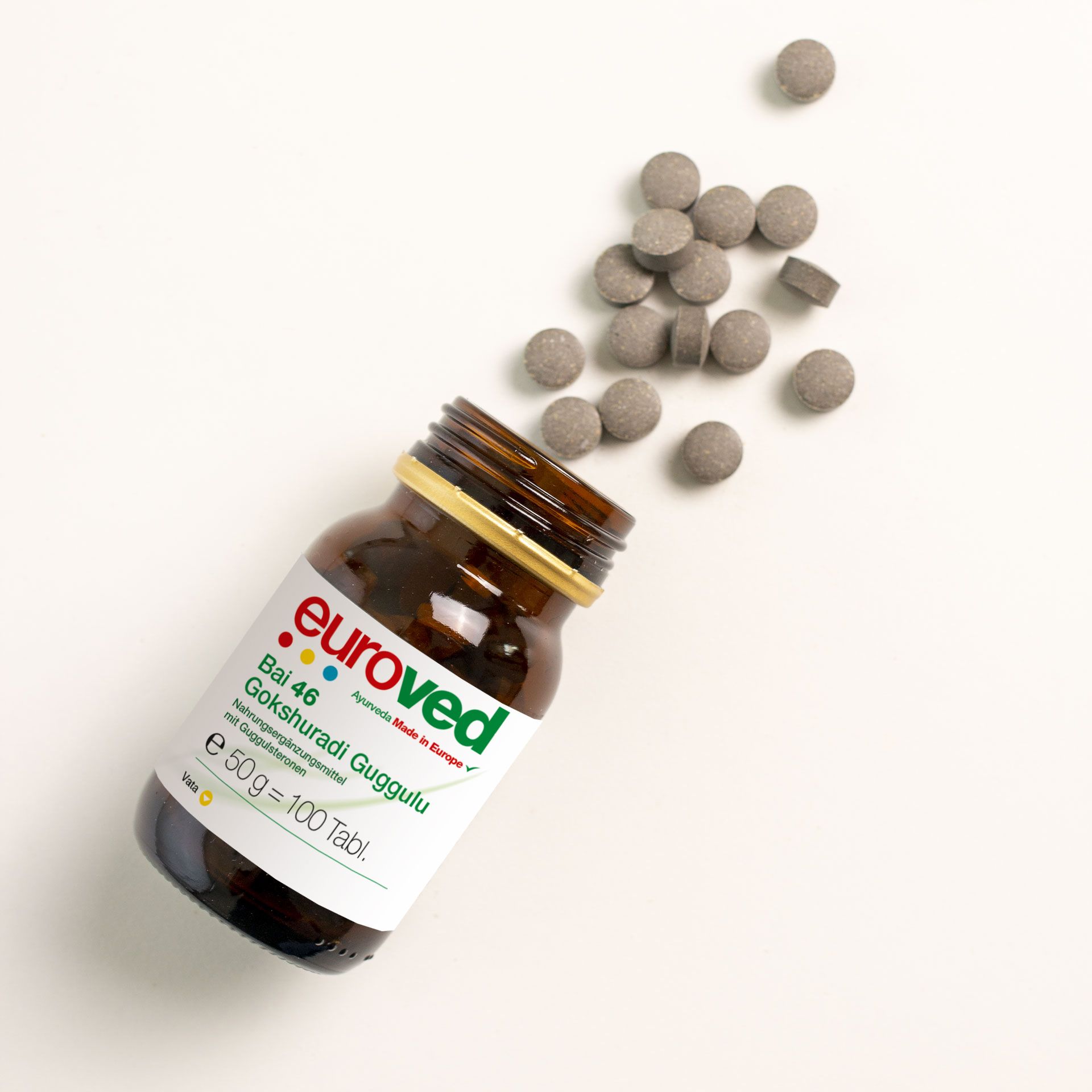 Braune Glasflasche mit Tabletten. Aufschrift: euroved, Bai 46, Gokshuradi Guggulu. Tabletten liegen daneben.