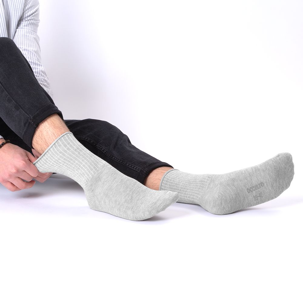 Person zieht graue Socke an. Rippstrickbündchen. Angenehmes Material. Füße auf hellem Hintergrund.