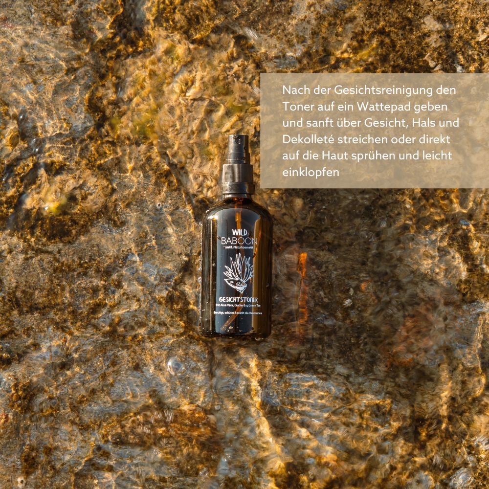 Braune Sprühflasche. Text: Wild Baboon Gesichtstoner. Auf Felsen. Wasser im Hintergrund.