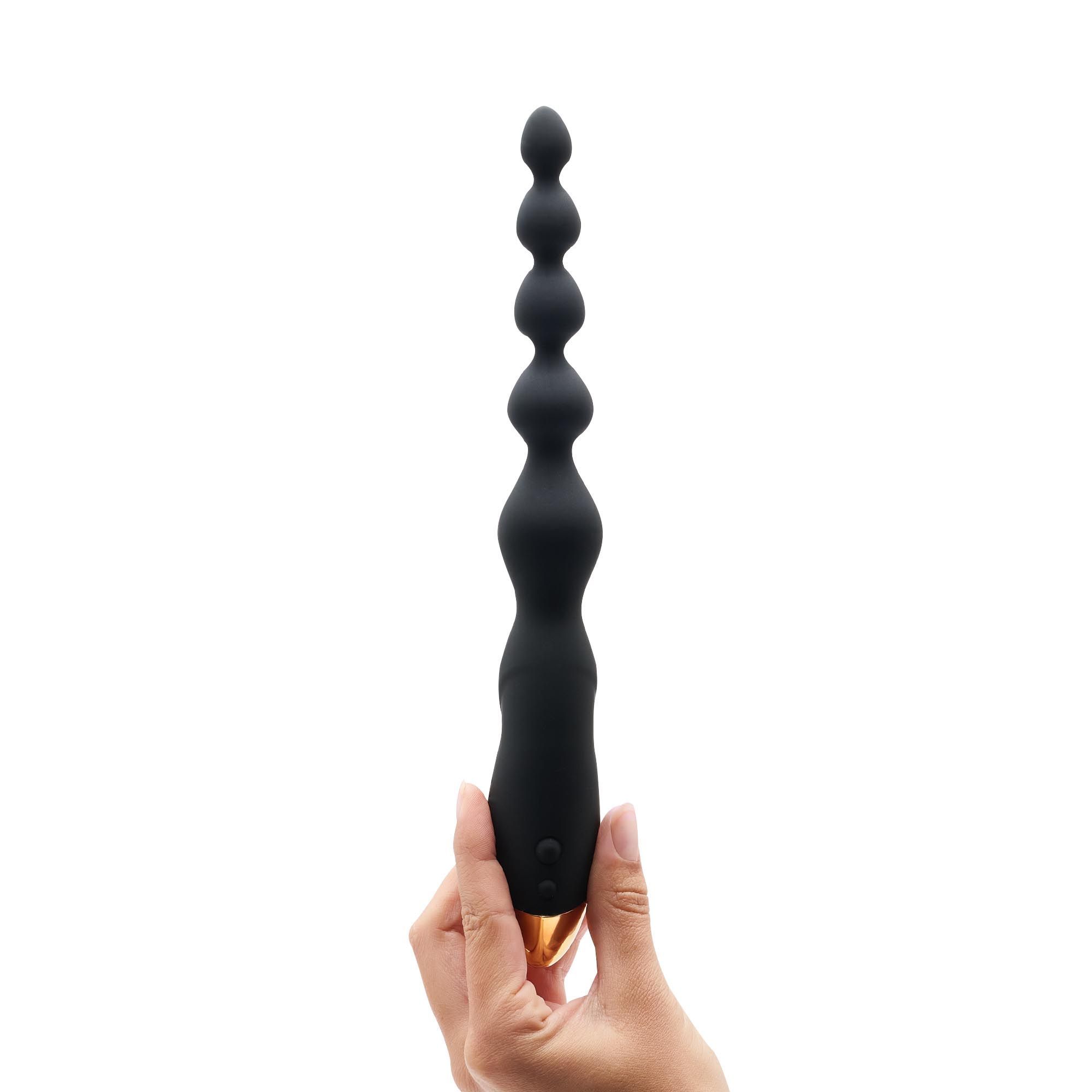 Schwarze, vibr. Anal-Kette mit goldfarbenem Ende, wird von einer Hand gehalten. Mehrere Kugeln.