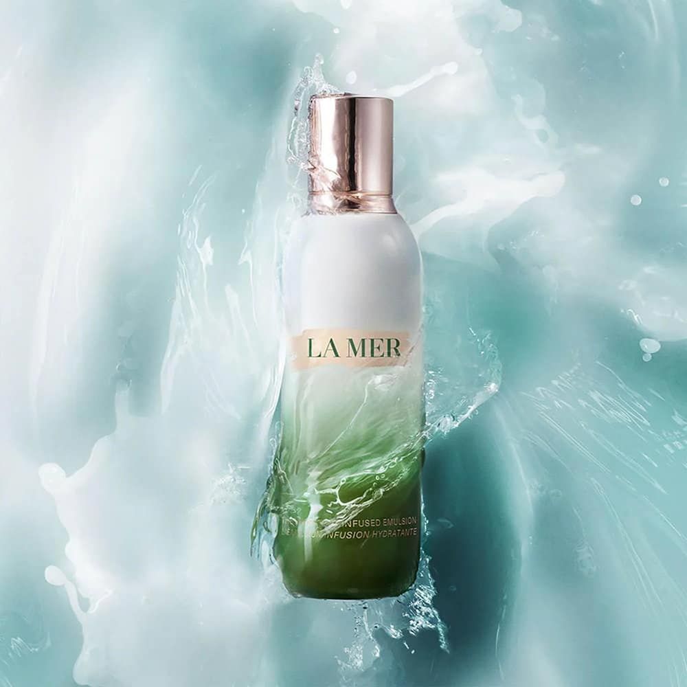 Weiße und grüne Flasche mit goldfarbenem Deckel. "LA MER" Schriftzug. Wasser spritzt um die Flasche herum.