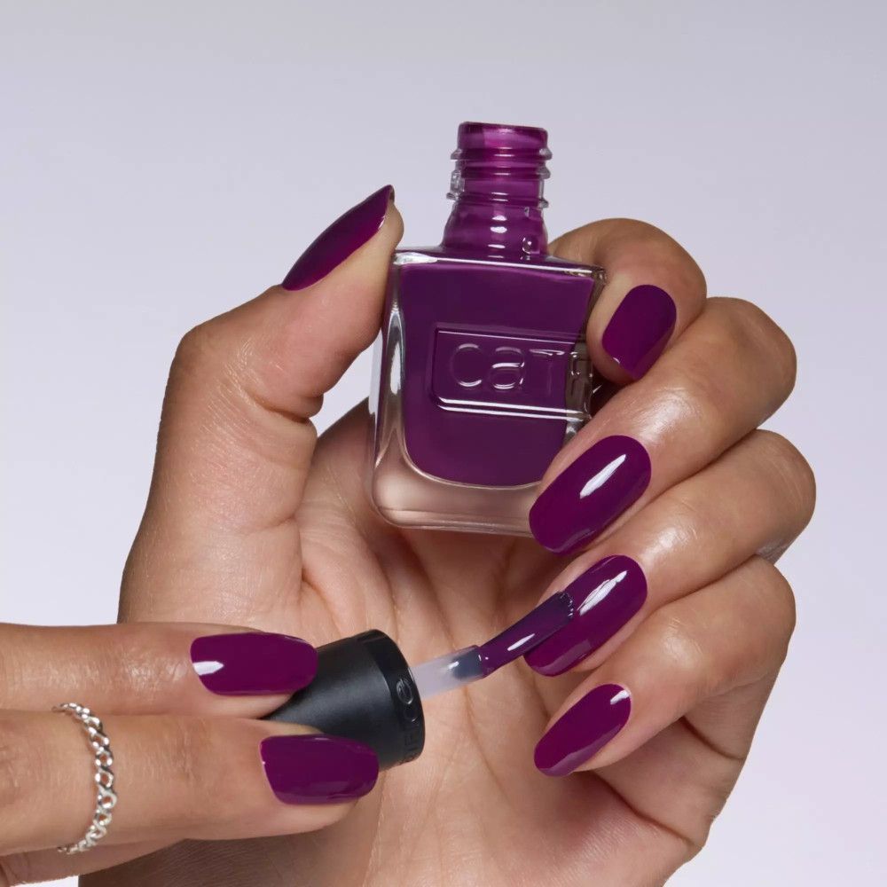 Hand mit lackierten Nägeln in dunklem Violett. Nagellackflasche und Pinsel. Catrice-Logo sichtbar.