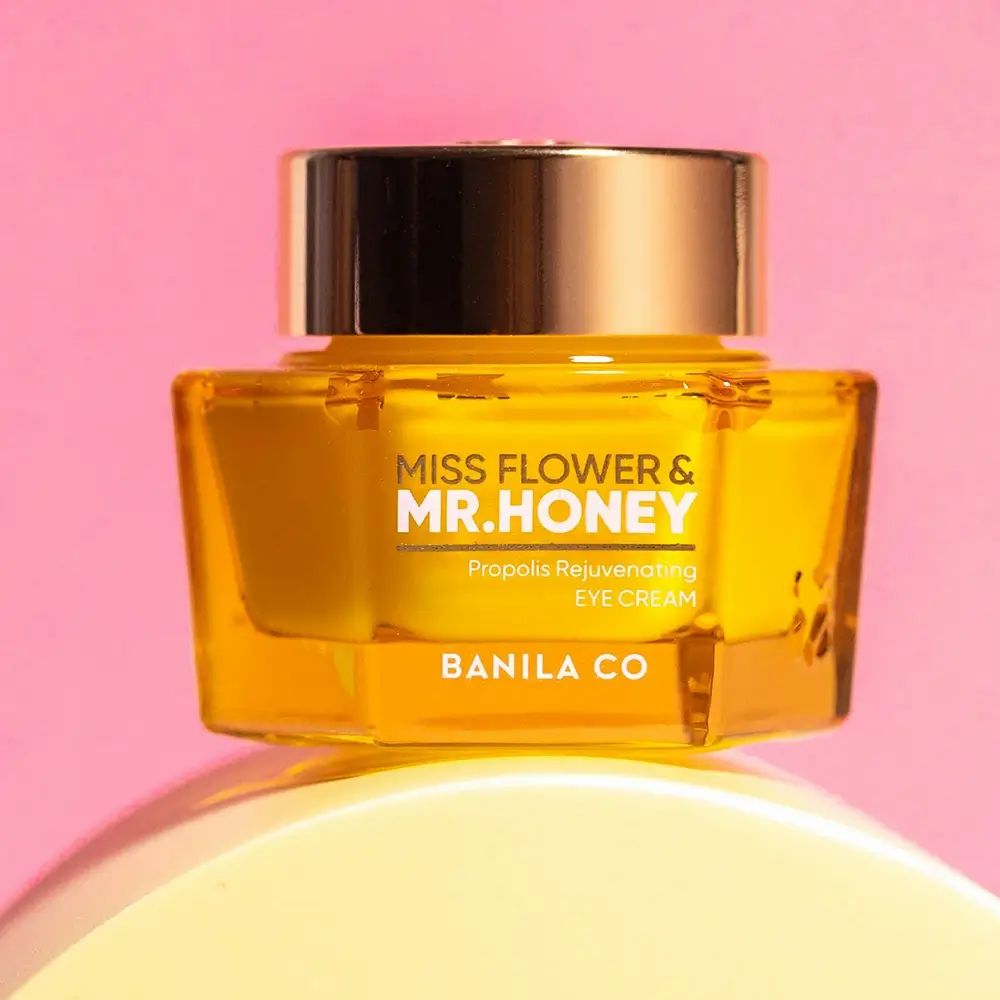 Gelber Tiegel mit goldenem Deckel. Aufschrift: MISS FLOWER & MR. HONEY, Propolis Rejuvenating EYE CREAM, BANILA CO. Auf gelbem Podest.