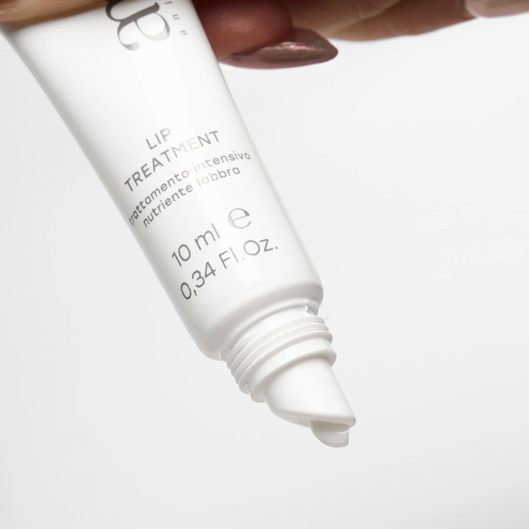 Primo piano di un tubo bianco per il trattamento labbra. L'applicatore è visibile. Il tubo riporta "am" e "LIP TREATMENT".