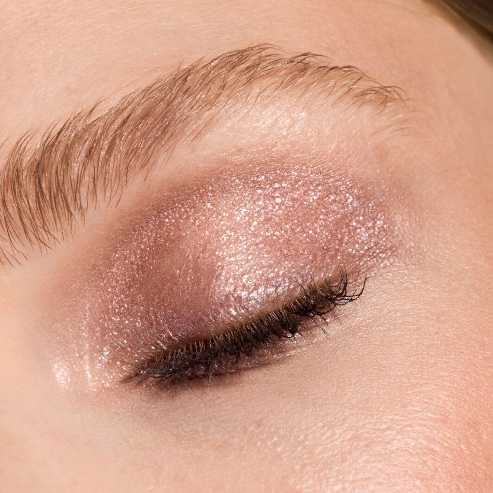 Nahaufnahme eines geschminkten Auges. Lidschatten in Rosa- und Goldtönen. Wimpern und Augenbrauen sichtbar.