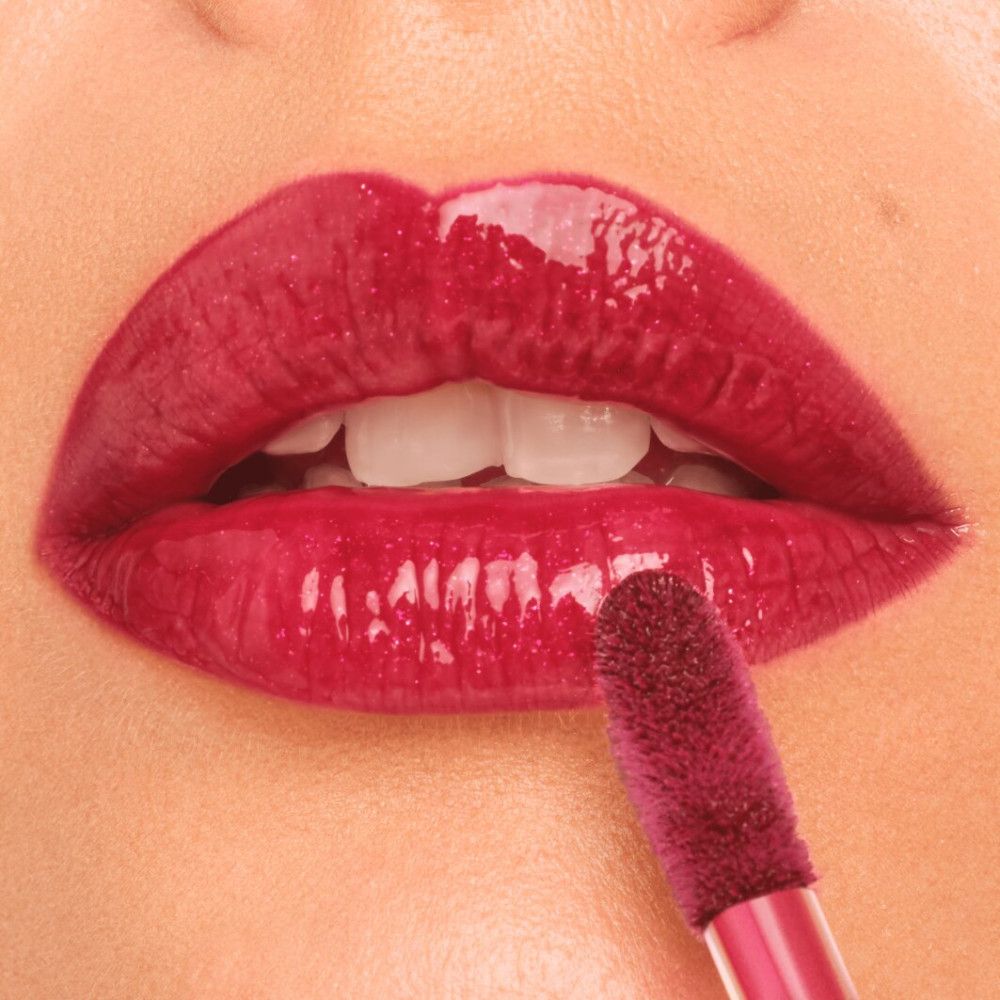 Nahaufnahme von Lippen mit aufgetragenem, glänzendem Lipgloss. Ein Applikator ist zu sehen.