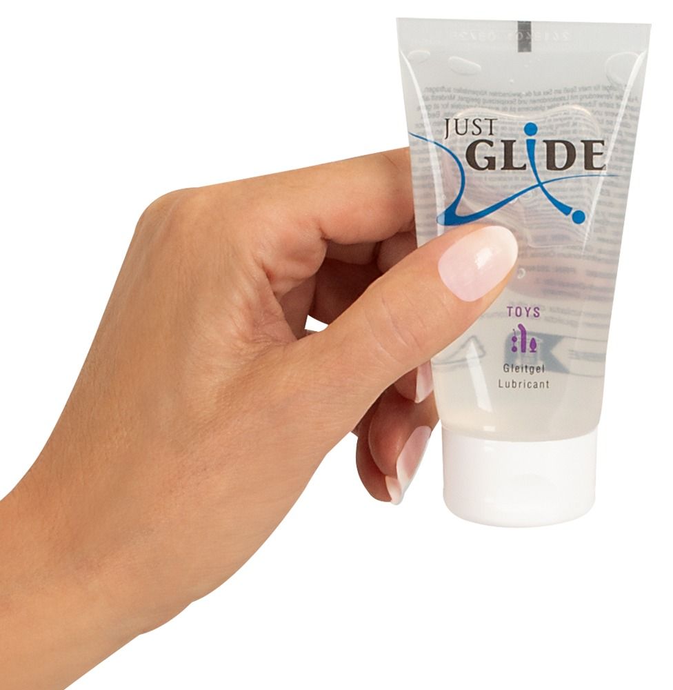 Hand hält Tube "JUST GLIDE TOYS". Die Tube ist transparent und enthält Gleitgel. Der Tubenkopf ist weiß.