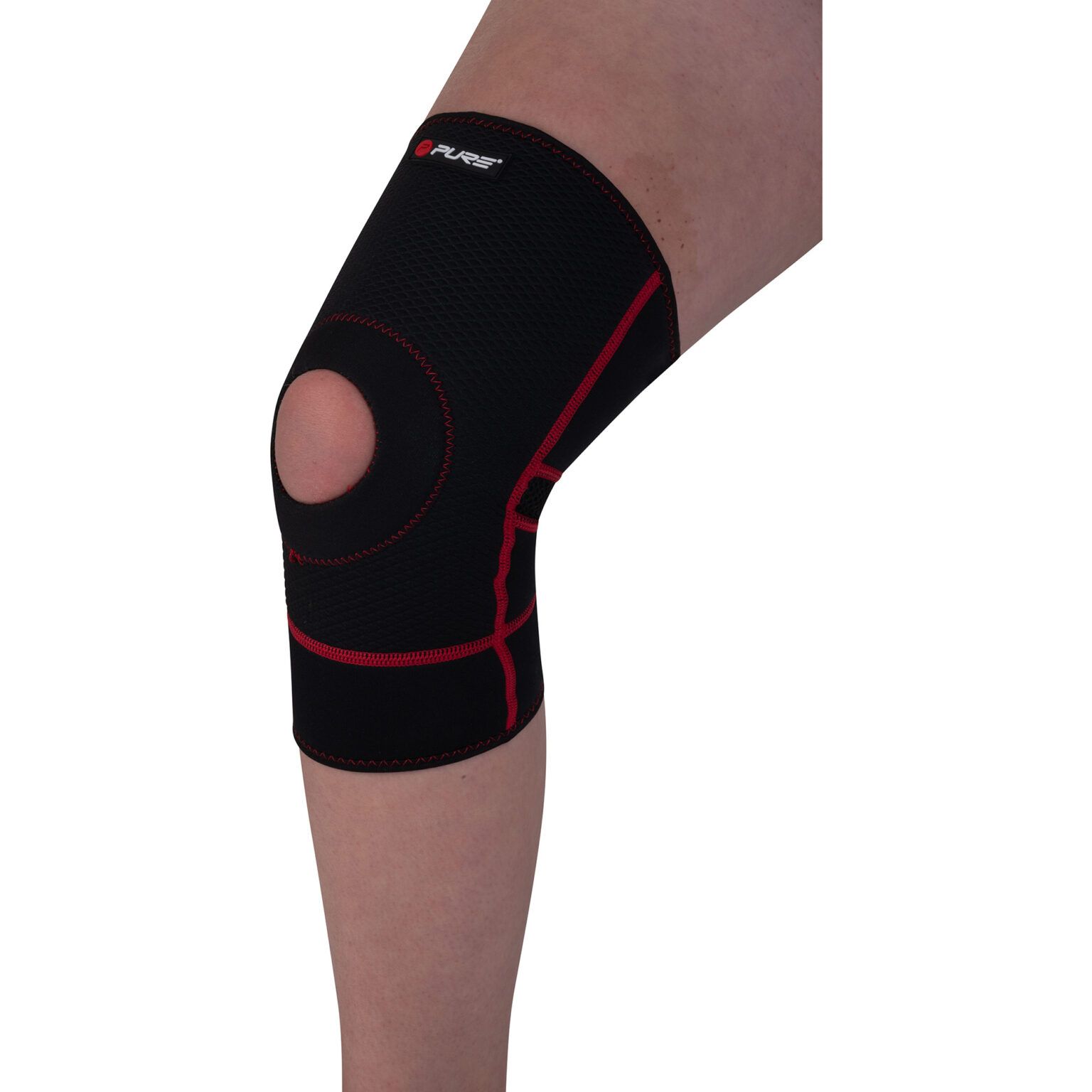 Il tutore per ginocchio Pure2Improve, in neoprene nero con cuciture rosse, è indossato su una gamba. La rotula aperta è ben visibile. Il logo Pure è visibile in alto. Il tutore offre supporto.