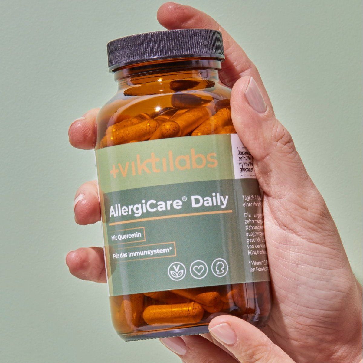 Hand hält braune Glasflasche mit AllergiCare® Daily Kapseln. Aufschrift: Quercetin, Für das Immunsystem. Siegel und Logos.