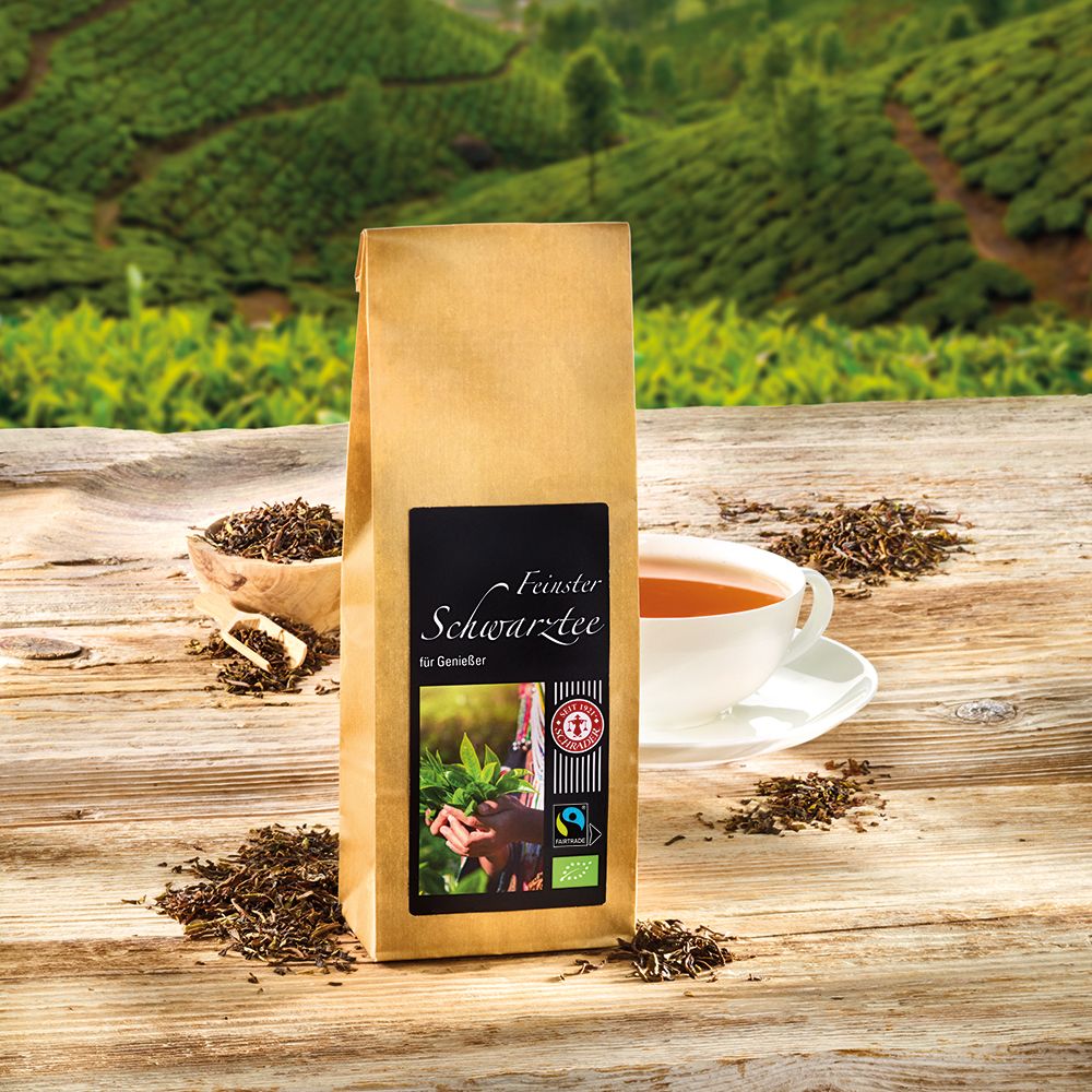 Braune Papiertüte mit schwarzem Etikett. Aufschrift: Feinsten Schwarzer Tee. Tee und Tasse auf Holzoberfläche.