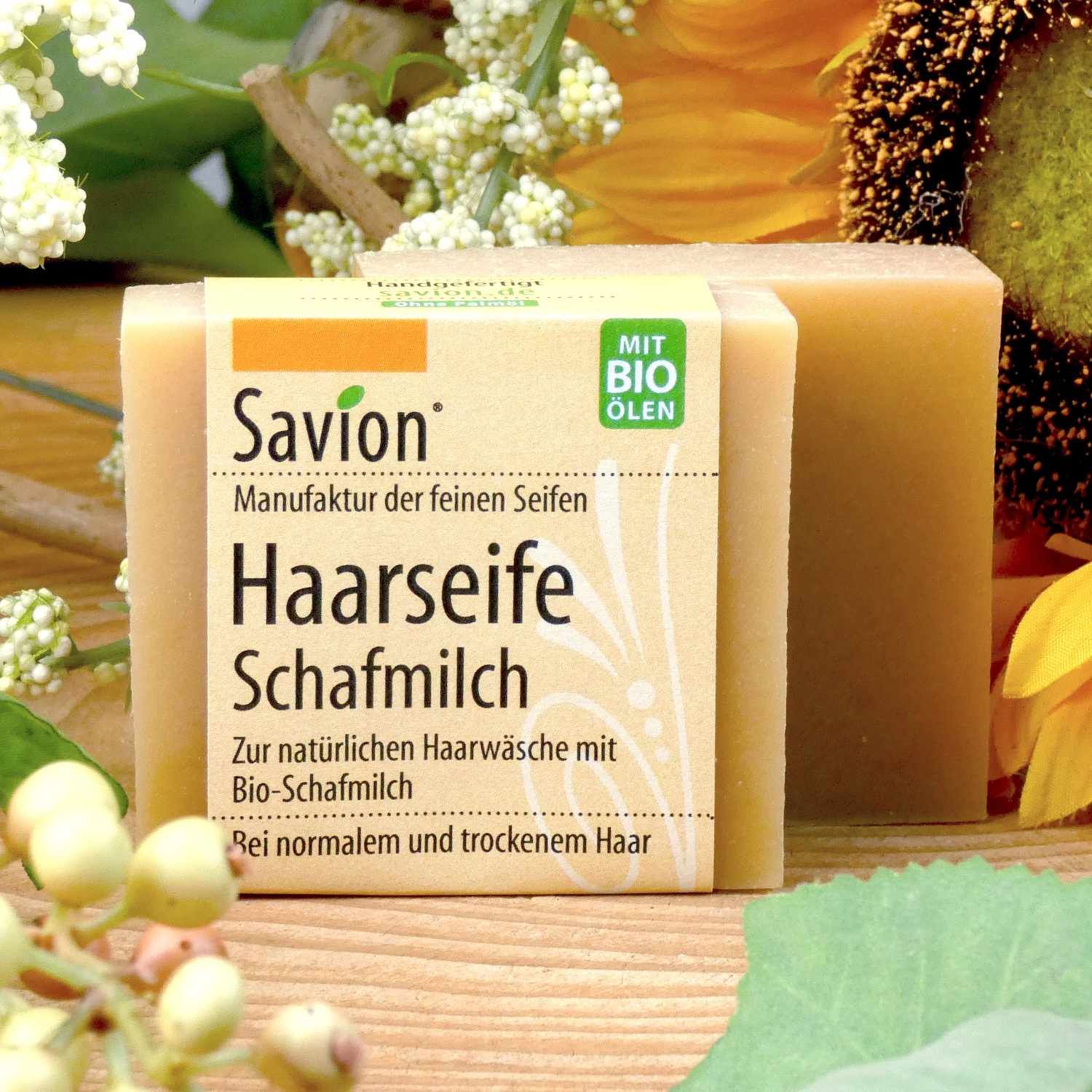 Zwei rechteckige Seifenstücke mit Papierbanderole. Auf der Banderole steht "Savion Haarseife Schafmilch" und "Mit Bio Ölen".
