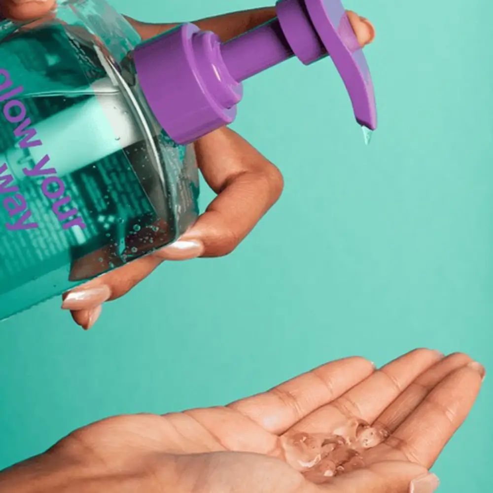 Hand hält Flasche mit lila Pumpe. Gel wird in die andere Hand gegossen. Aufschrift: "glow your own way". Hintergrund türkis.
