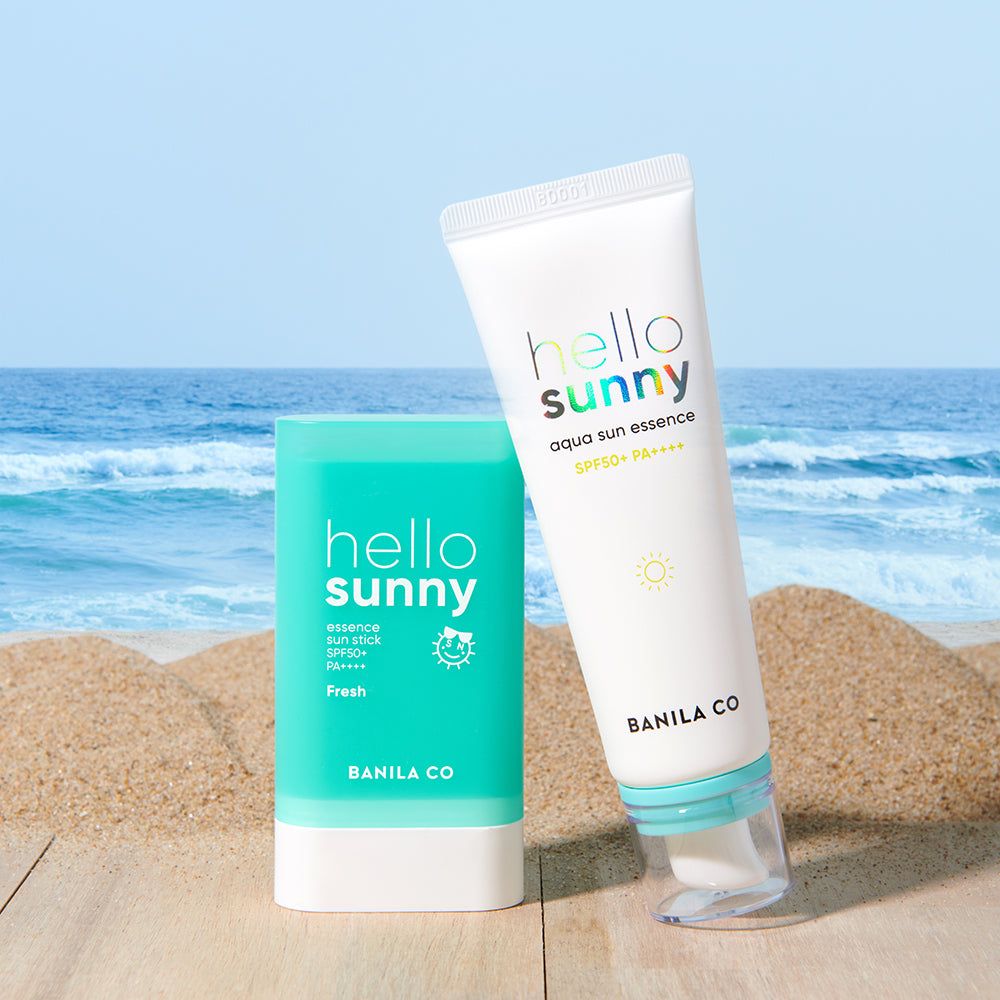 Zwei Banila Co. Hello Sunny Sonnenschutzprodukte: ein Sonnenspray und ein Sonnenschutzstift auf einer Strandkulisse.