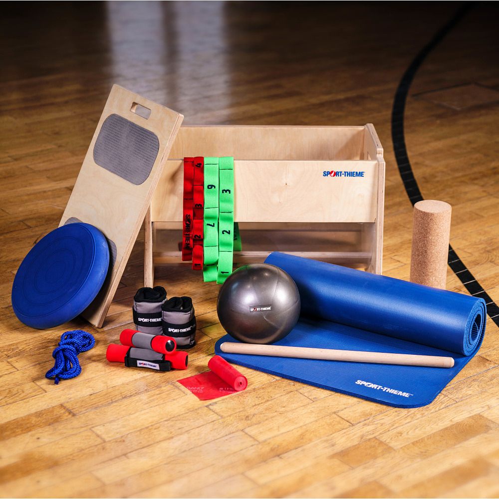 Trainingsgeräte neben der Movebox aus Holz mit Sport-Thieme Logo. Enthält Bälle, Matten, Bänder und Gewichte.