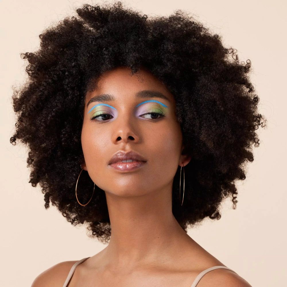 Porträt einer Frau mit Locken und farbigem Augen-Make-up. Goldene Creolen.