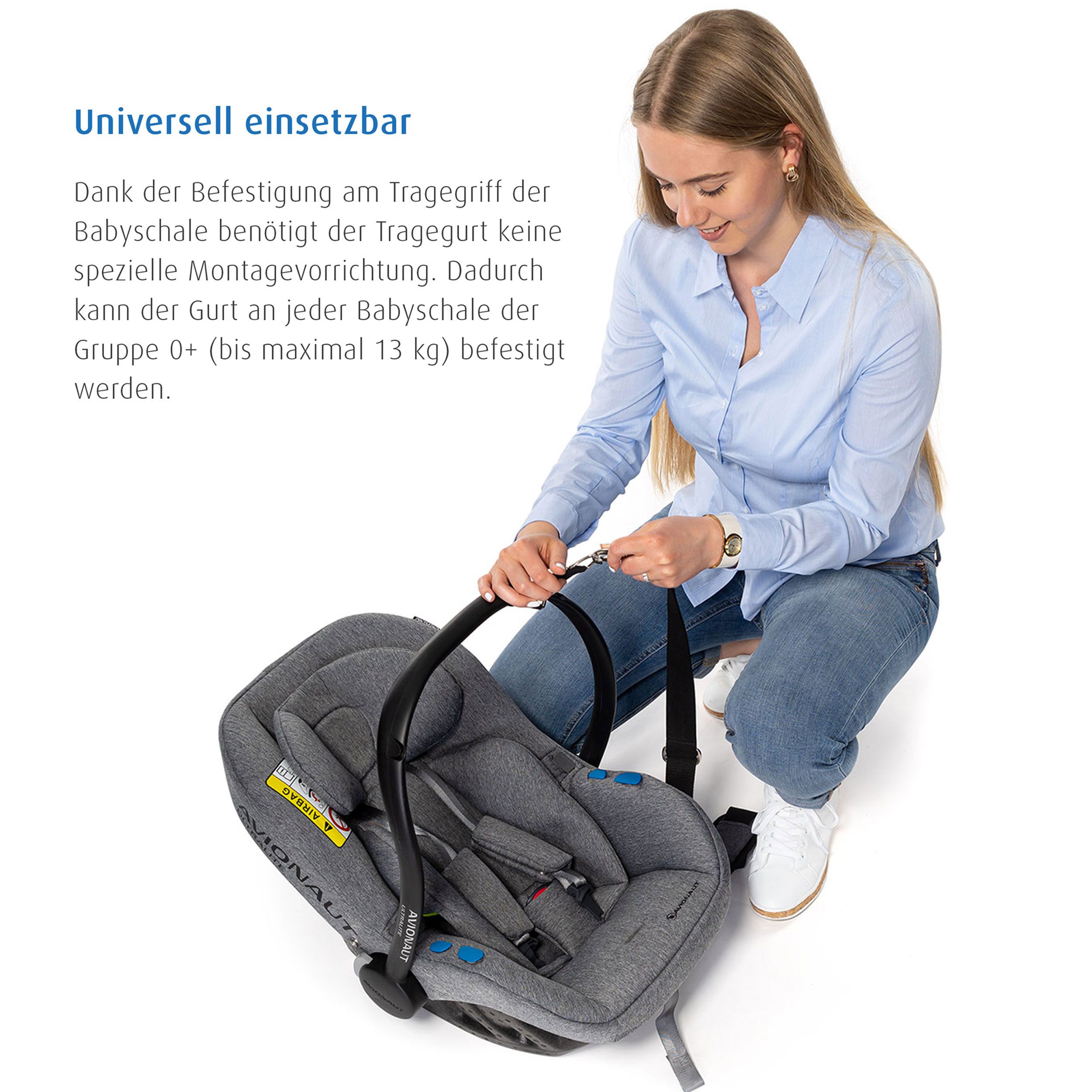 Eine Frau befestigt den Tragegurt an einer Babyschale. Der Gurt ist schwarz.