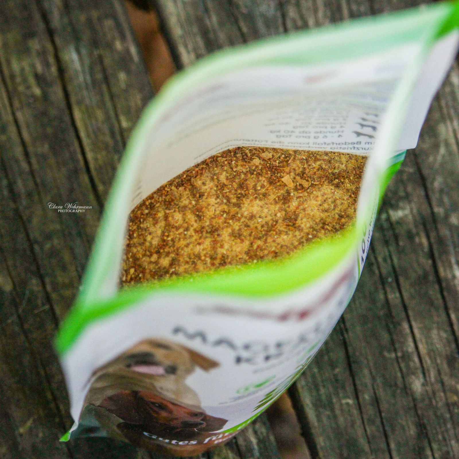 Geöffnete Tüte Stiefel Magen-Darm-Kräuter. Inhalt: braunes, körniges Produkt. Verpackung mit grünem Akzent, auf Holzuntergrund.