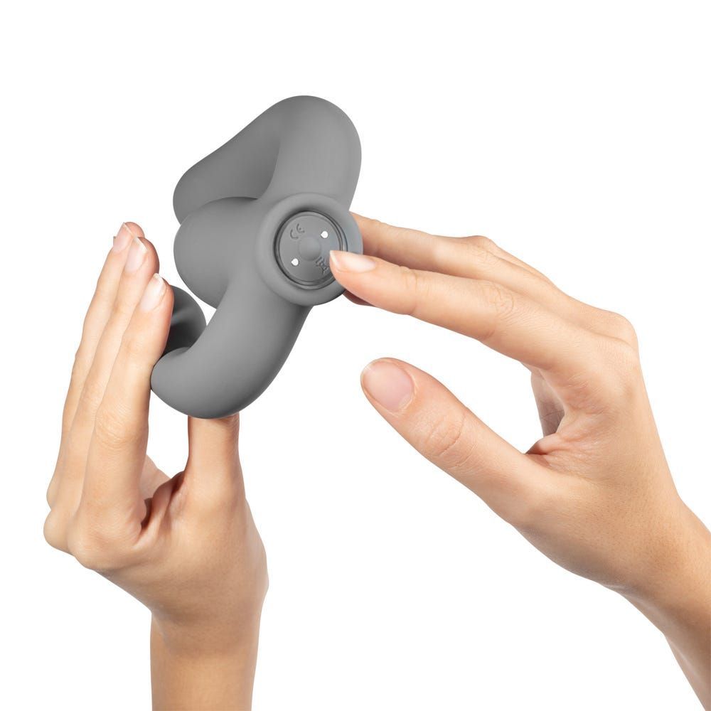Grauer Vibrator, gehalten von zwei Händen. Ein Knopf ist sichtbar. Das Produkt hat eine geschwungene Form.