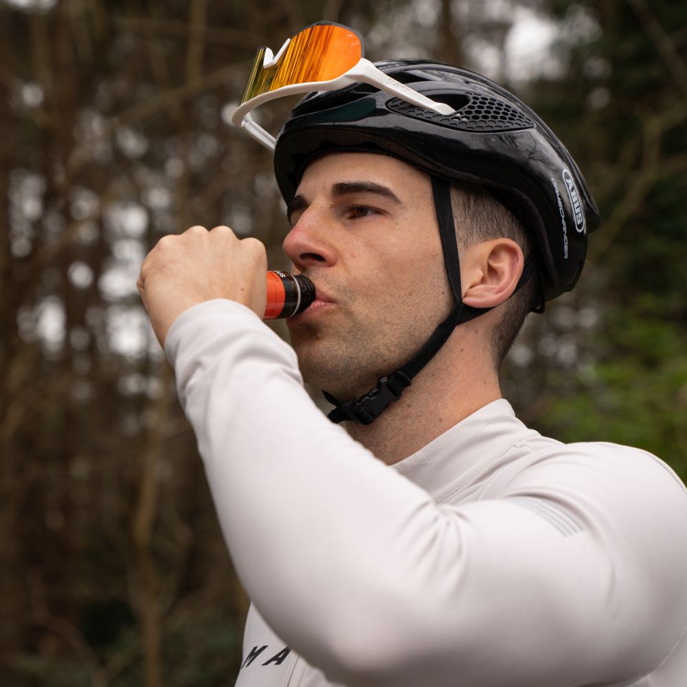 Mann trinkt aus einer Flasche OLEUS Pre-Activity Endurance Shot. Er trägt eine Sonnenbrille und einen Helm.