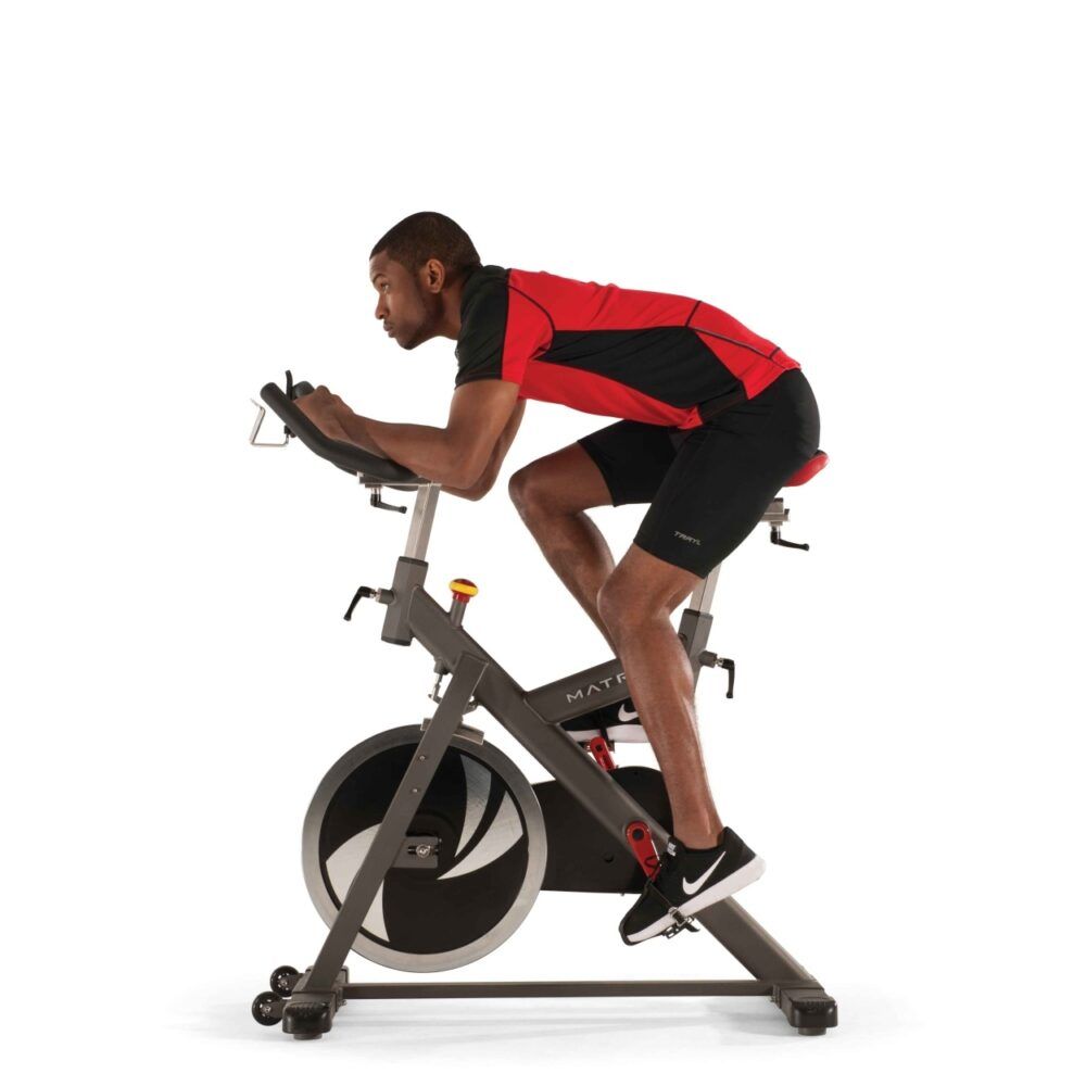 Indoor Cycle. Grauer Rahmen, schwarze Lenkstange, roter Sattel. Person trainiert. Person in Trainingsposition.