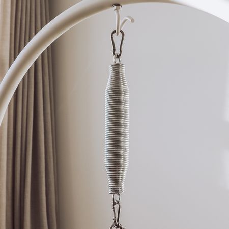 Metallfeder mit Karabinern, an einem weißen Gestell befestigt. Im Hintergrund Vorhang.