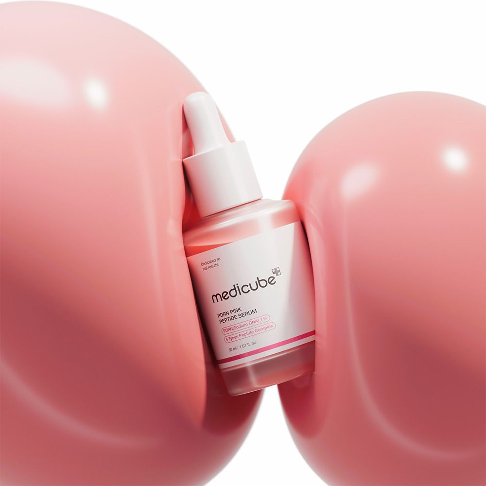 Medicube PDRN Pink Peptide Serum Flasche zwischen zwei großen rosa Kugeln.