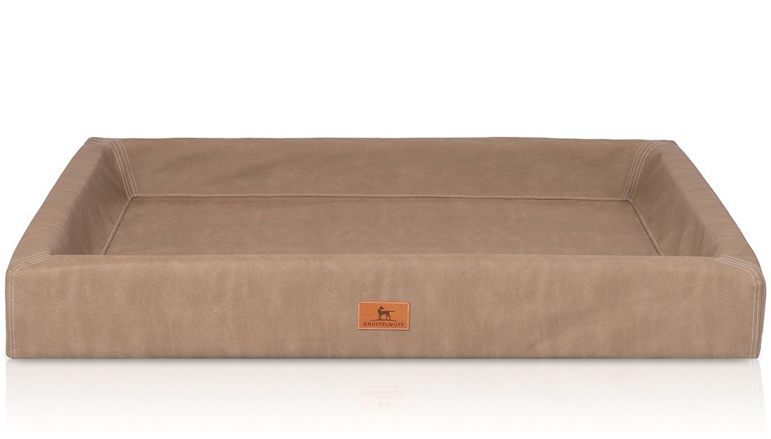 Beiges orthopädisches Hundebett. Rechteckige Form mit erhöhtem Rand. Logo-Patch an der Vorderseite.