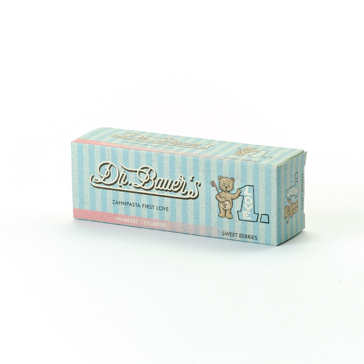 Kartonverpackung für Zahnpasta. Hellblau mit rosa Streifen. Aufschrift: Dr. Bauer's Zahnpasta First Love Sweet Berries. Abbildung eines Bären.