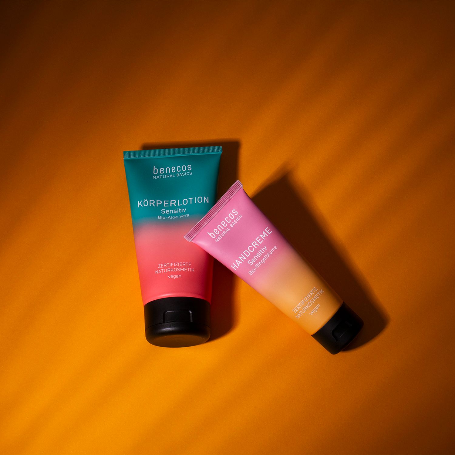 Zwei Benecos Tuben: Handcreme Sensitiv Bio-Ringelblume und Körperlotion Sensitiv Bio-Aloe Vera. Auf orangefarbenem Hintergrund.