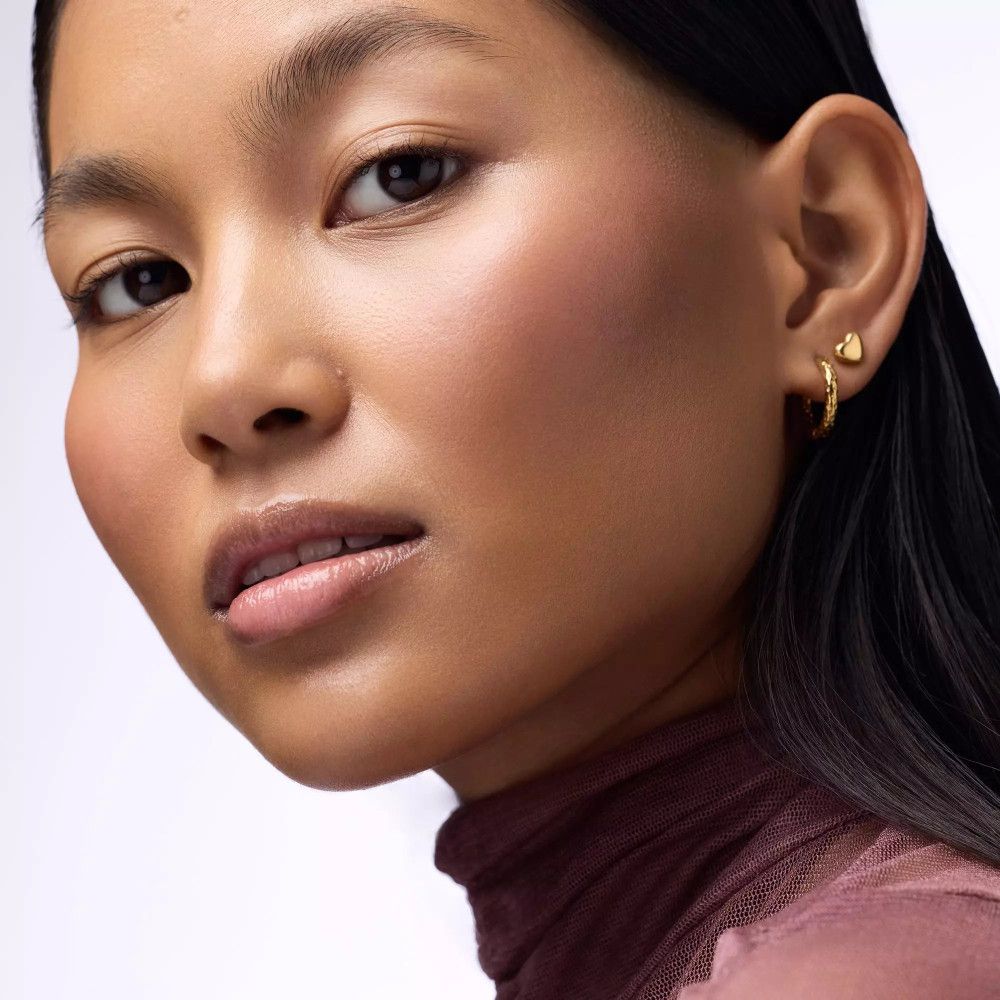 Nahaufnahme einer Frau mit gebräunter Haut. Sie trägt goldene Ohrringe. Ihr Blick ist nach oben gerichtet.